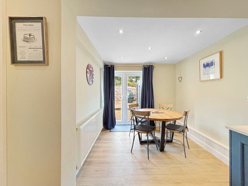 Bright dining room with wooden table, chairs, glass doors to garden, and cream walls