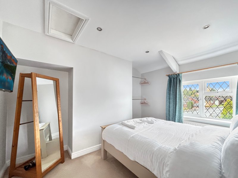 Bright bedroom with double bed, wooden door frame, leaded-glass window and teal curtains