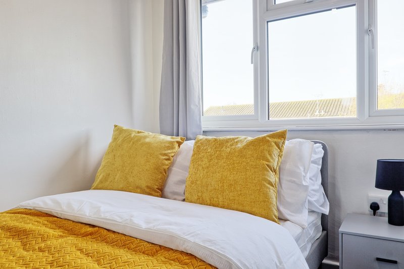 Bright bedroom with double bed, yellow pillows and bedding, large windows overlooking fields