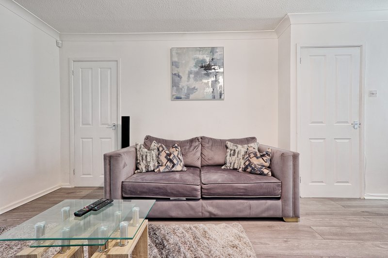 Modern living room with mauve sofa, glass coffee table, framed artwork and white doors