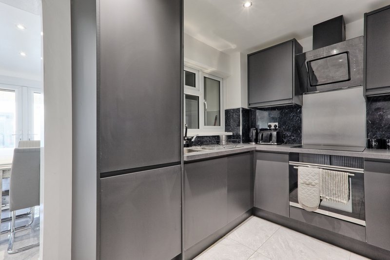 Modern kitchen with grey cabinetry, black granite countertop, stainless steel appliances and white floor