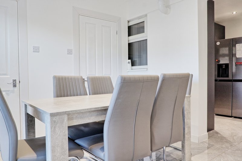 Modern dining area with grey upholstered chairs and light wood table in open-plan kitchen space