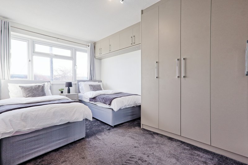 Bright bedroom with two single beds, built-in wardrobe, and large window overlooking garden