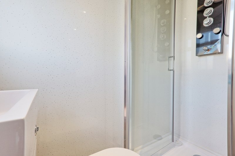 Small modern bathroom with toilet, sink, shower enclosure and wall storage