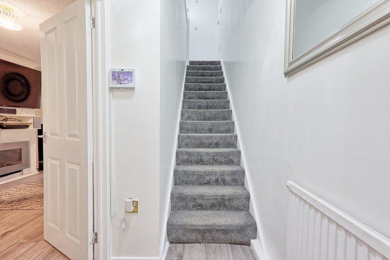 Staircase with gray carpet runner, white walls, and wooden flooring visible in hallway.