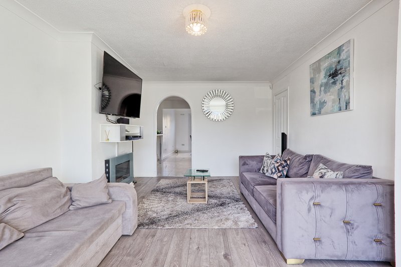 Open-plan living room with two purple sofas, wooden floor, wall-mounted TV, and modern decor