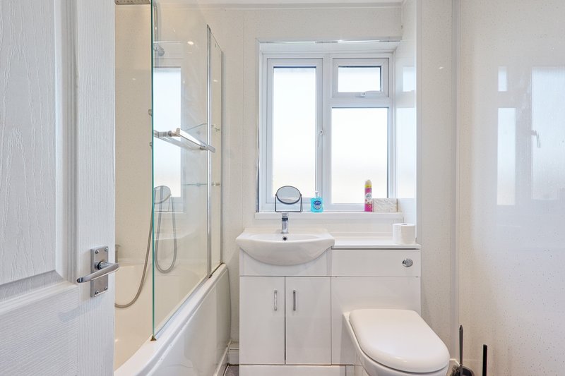 Clean modern bathroom with white vanity, sink, toilet, shower enclosure and window