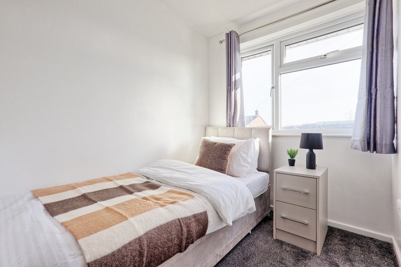 Bright bedroom with double bed, brown and cream bedding, bedside table, lamp and window view