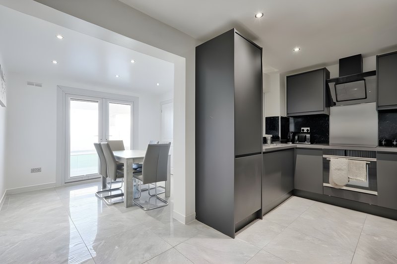 Modern open-plan kitchen and dining area with black cabinetry, stainless steel appliances, and light tile flooring