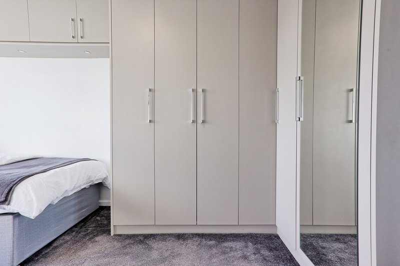 Bedroom with single bed, large white built-in wardrobes and dark carpet flooring