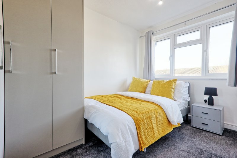 Bright bedroom with double bed, yellow bedding, white wardrobe, and large window