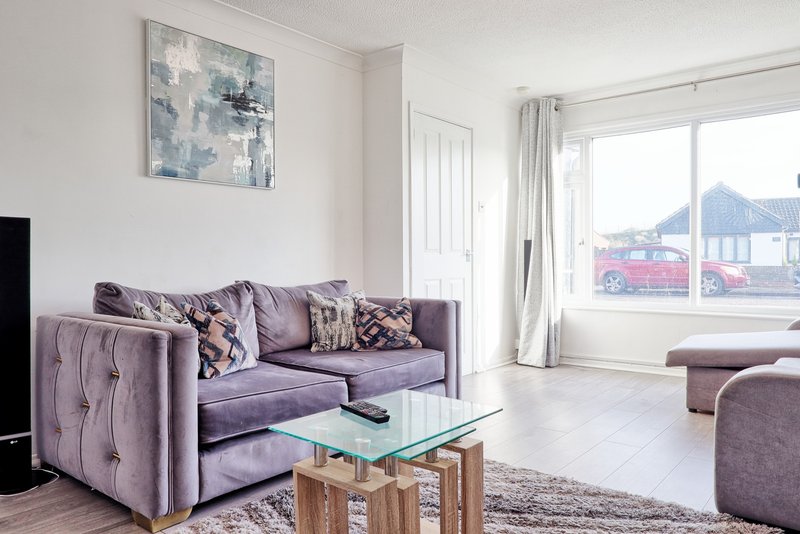 Modern living room with purple sofa, glass coffee table, abstract wall art and large windows