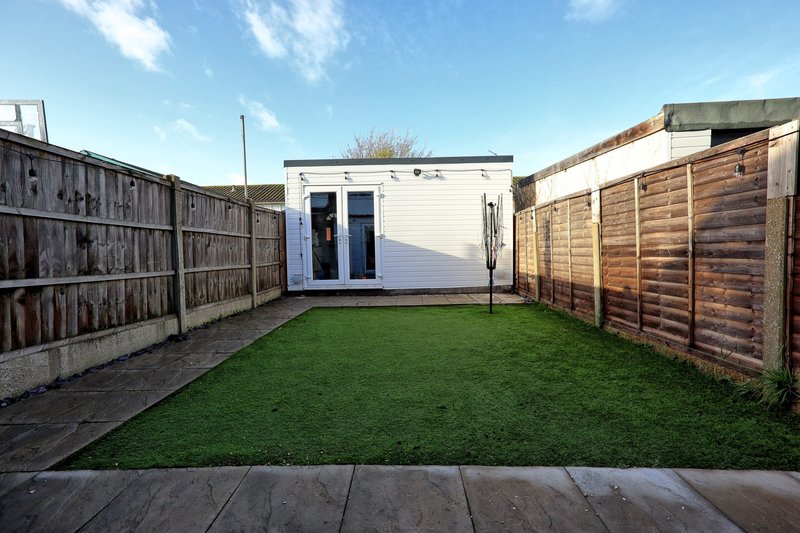 Modern garden with artificial turf, white garden building, wooden fences and paved patio