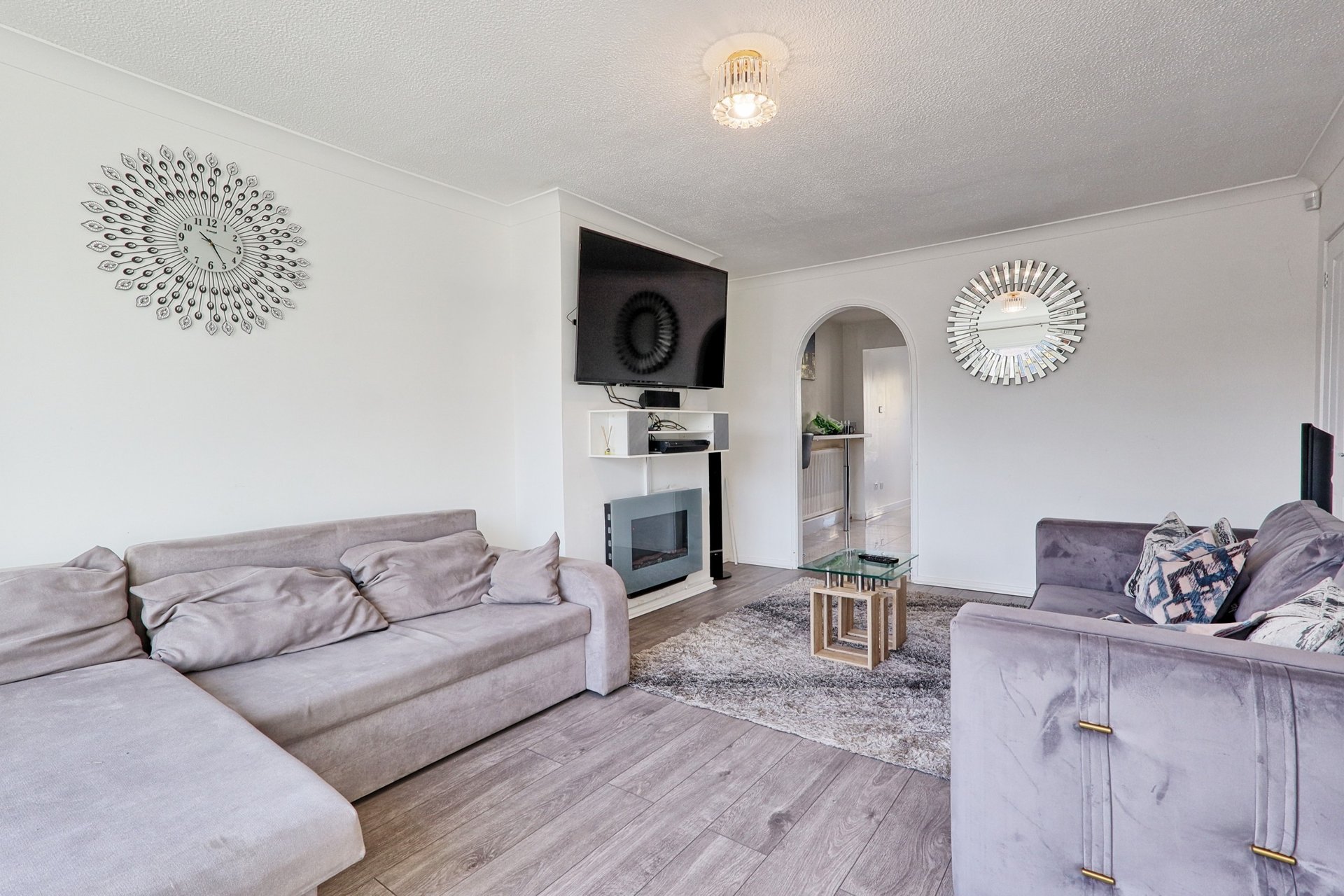 Living room with gray sofas, wall-mounted TV, fireplace, and decorative wall mirrors