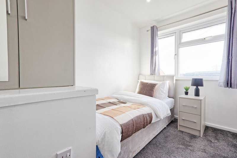 Bright bedroom with single bed, white furniture, window with purple curtains, and bedside lamp