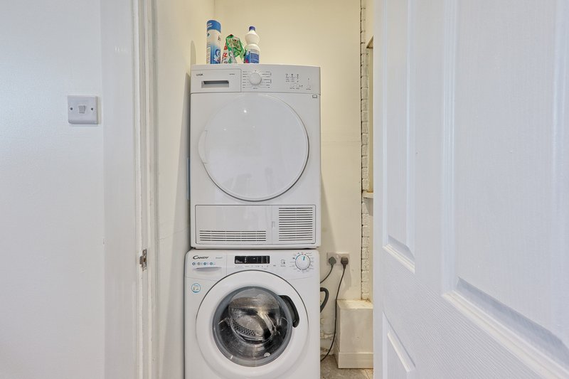 Stacked white washing machine and tumble dryer in utility room with detergent bottles