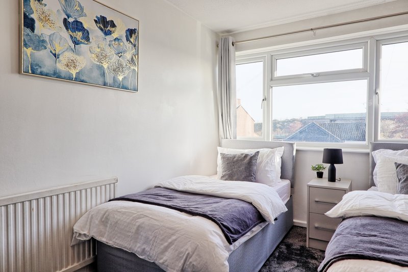Bright bedroom with two single beds, radiator, large window with mountain views, and framed artwork