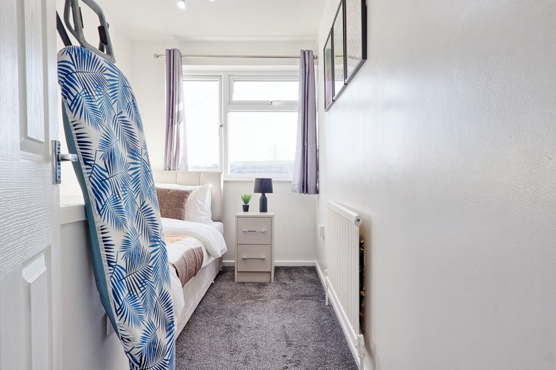 Narrow bedroom with single bed, patterned blue throw, bedside table and window with curtains