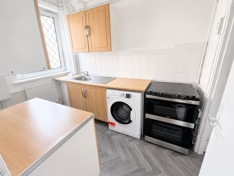 Kitchen with wooden cabinets, sink, washing machine, electric oven and wooden worktops