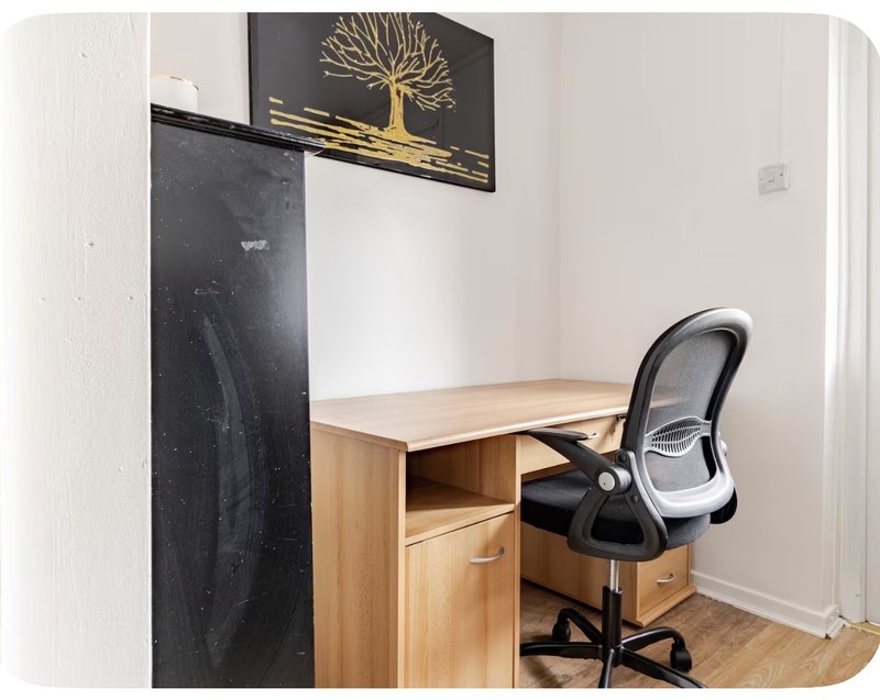 Home office workspace with wooden desk, black office chair, and decorative wall art