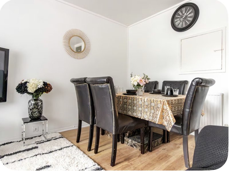 Dining room with round table, black leather chairs, floral arrangement, and decorative wall clock