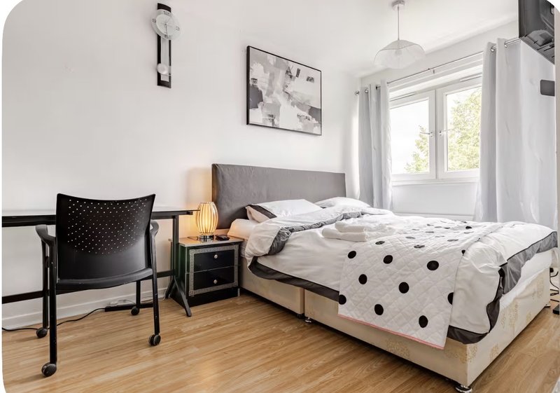 Bright bedroom with double bed, black chair, wooden floor and white curtains