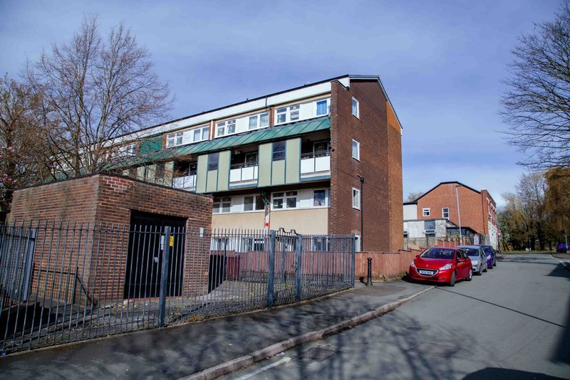 Brick apartment building with green trim, fenced forecourt, parked cars and bare trees