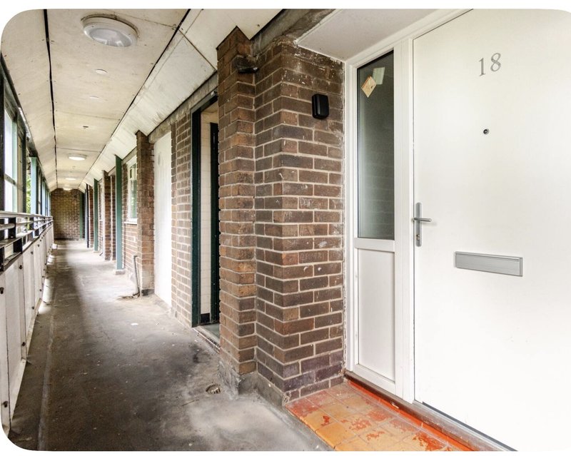 Exterior covered walkway with brick column, white door numbered 18, and residential entrance