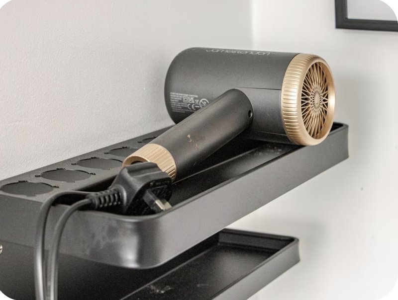 Hair dryer and styling tool stored on black wall-mounted shelf
