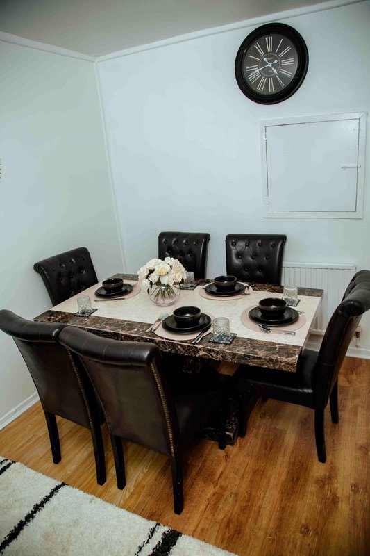 Dining room with black table, four upholstered chairs, place settings and wall clock