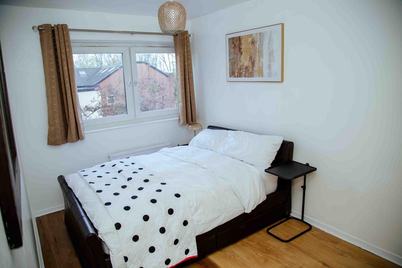 Bright bedroom with single bed, polka-dot duvet, wooden floor and window with brown curtains