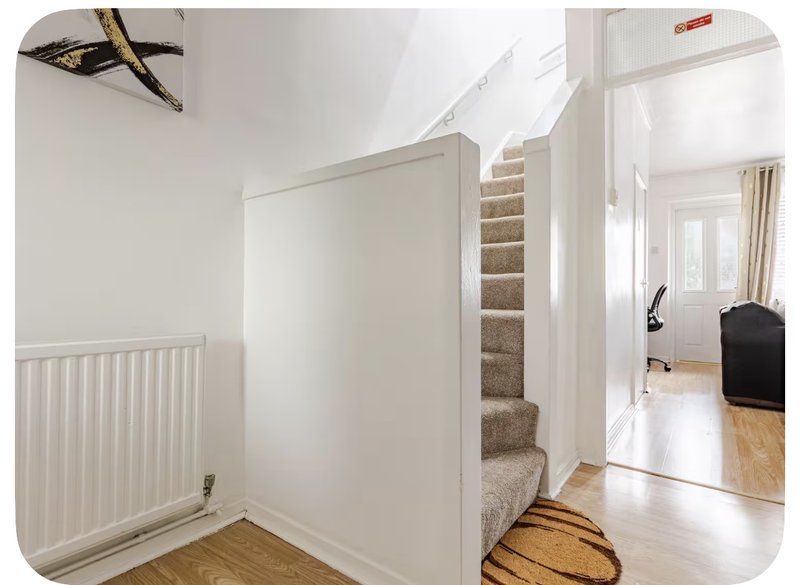 Bright hallway with white walls, radiator, staircase with beige carpet, and wooden flooring