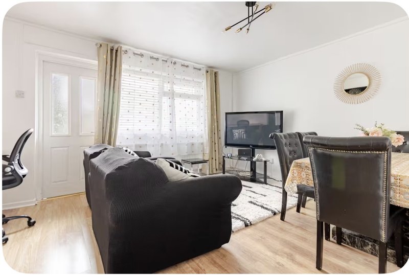 Bright living room with black sofa, TV, dining table, wooden flooring and patio doors