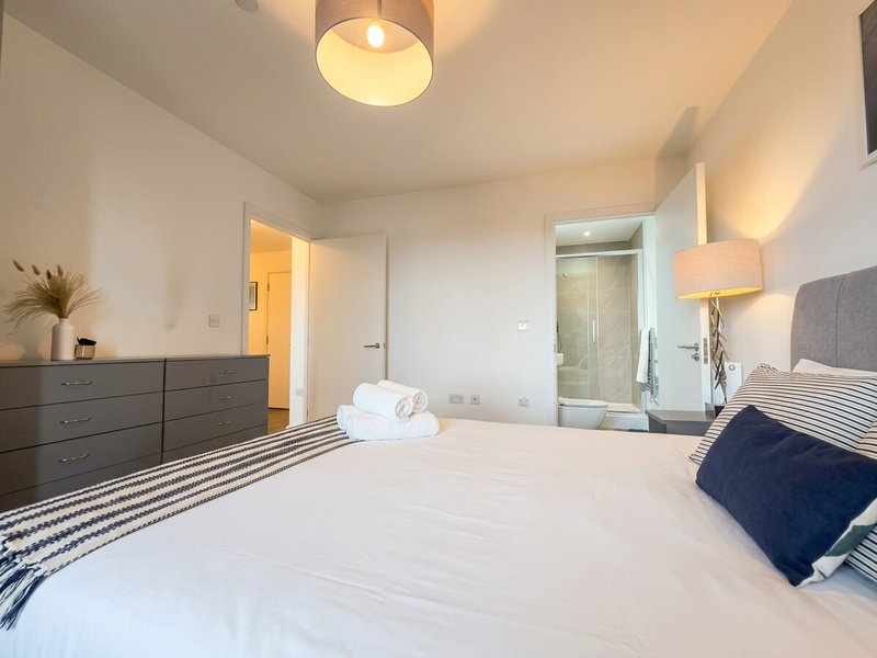 Modern bedroom with double bed, dark dresser, ensuite bathroom and ceiling light