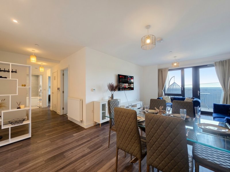 Modern open-plan apartment with dining area, lounge seating, and kitchen visible through archway