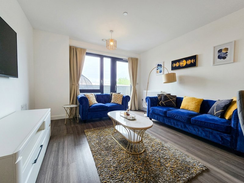 Modern living room with two blue velvet sofas, white coffee table, wooden flooring and large windows