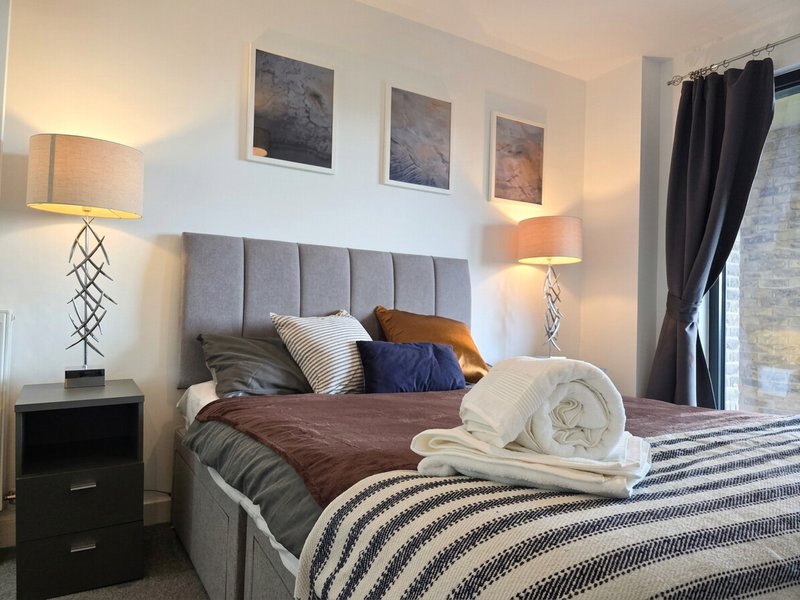 Modern bedroom with grey upholstered headboard, brown bedding, rolled towels and decorative pillows