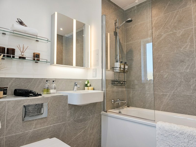 Modern bathroom with grey tile walls, illuminated mirror cabinet, white sink and shower enclosure