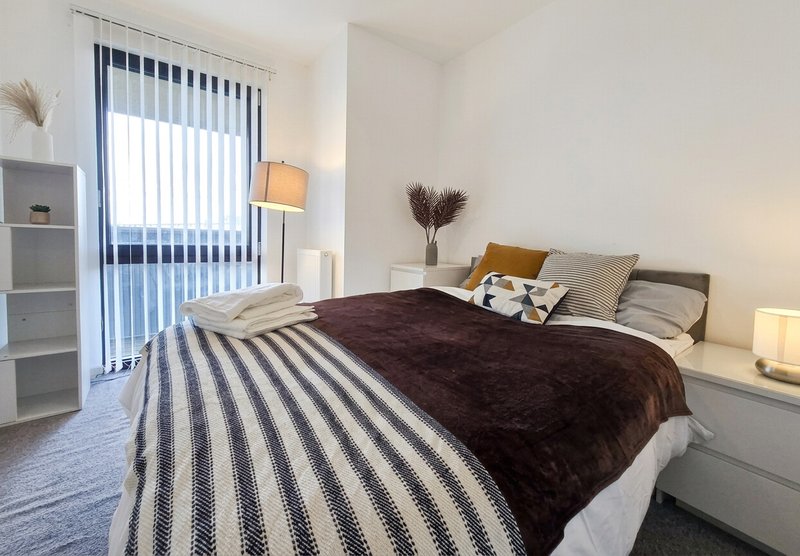 Modern bedroom with double bed, dark bedding, striped rug, and floor-to-ceiling windows with blinds