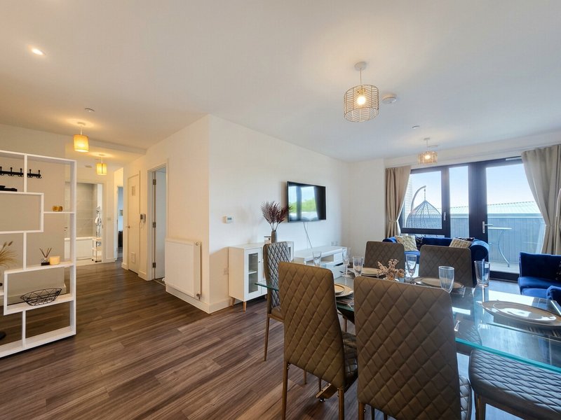 Modern open-plan apartment with dining area, comfortable seating, and floor-to-ceiling windows with balcony