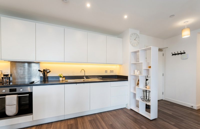 Modern white kitchen with black countertop, stainless steel appliances and wooden flooring