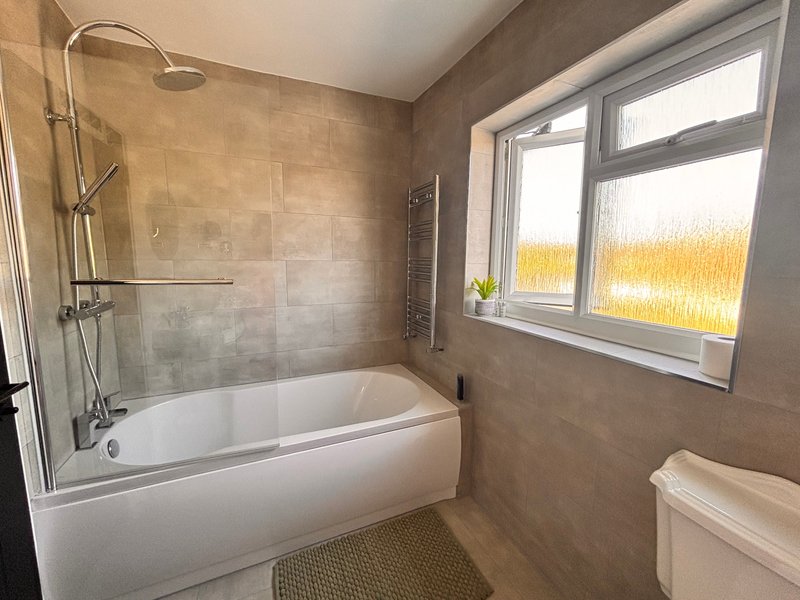 Modern bathroom with bathtub, glass shower screen, toilet and window with natural light main family bathroom