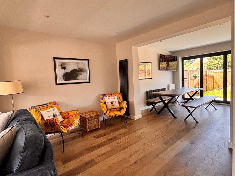 Open-plan living area with sofa, yellow armchairs, wooden flooring and garden view