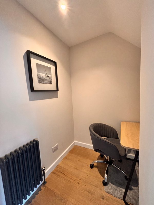 Small home office with black chair, wooden desk, framed artwork and radiator
