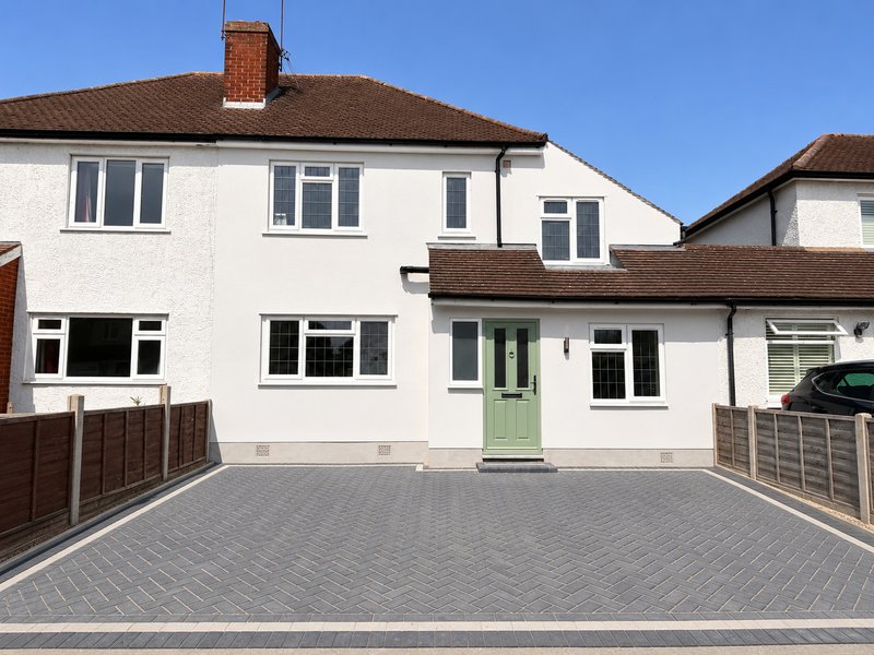 White semi-detached house with brown roof, driveway and green front door