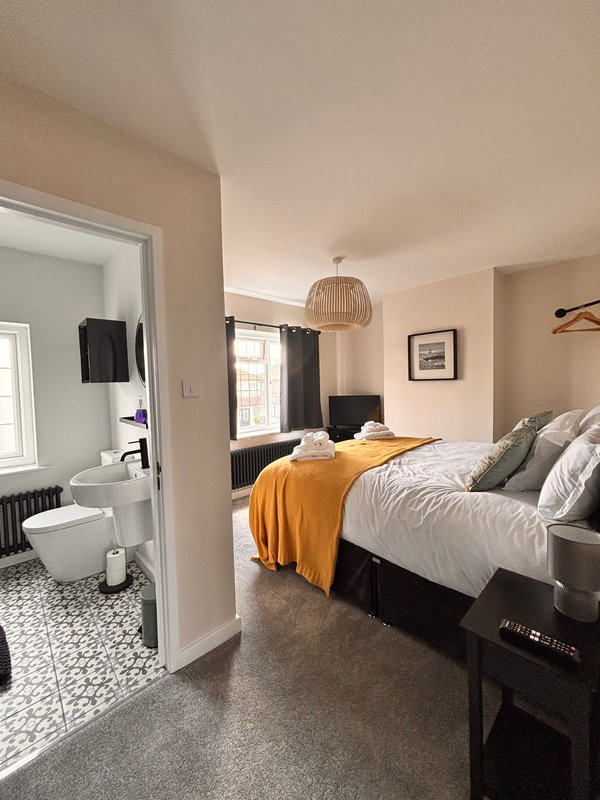 Modern bedroom with double bed, orange throw, ensuite bathroom visible through open door