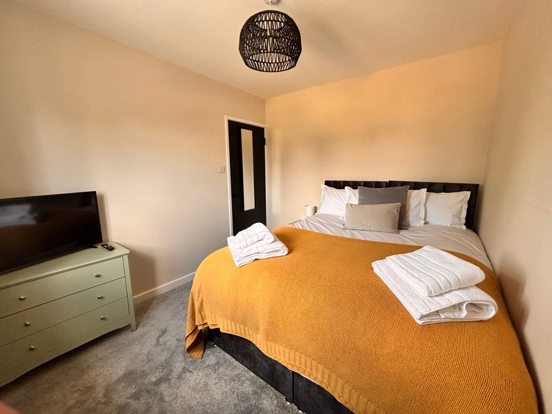 Bedroom with double bed, yellow blanket, white pillows, wooden dresser and pendant light