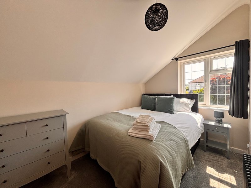 Bright attic bedroom with double bed, grey dresser, bedside table and large window