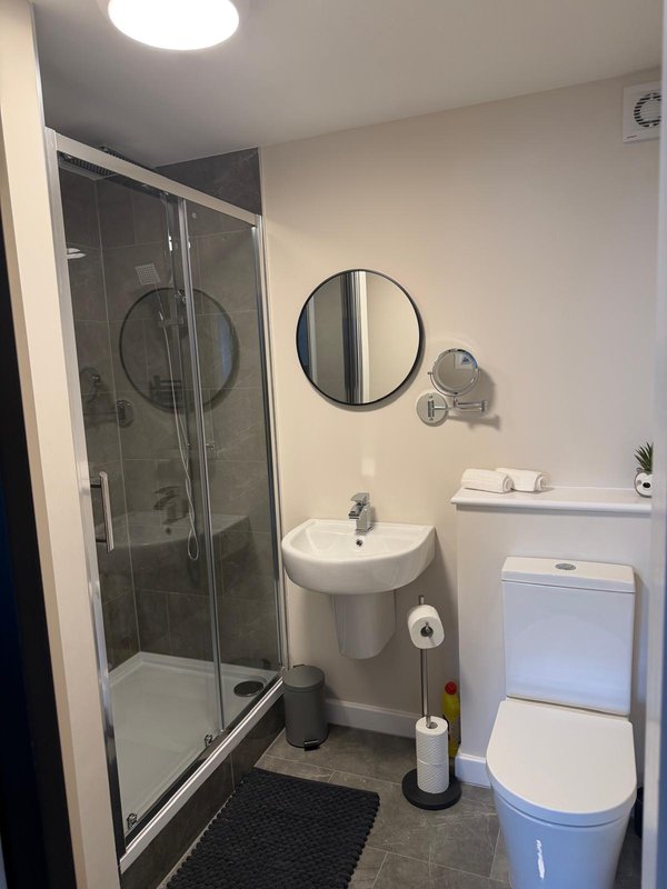 Modern bathroom with shower enclosure, pedestal sink, toilet and round mirror ensuite to room 5