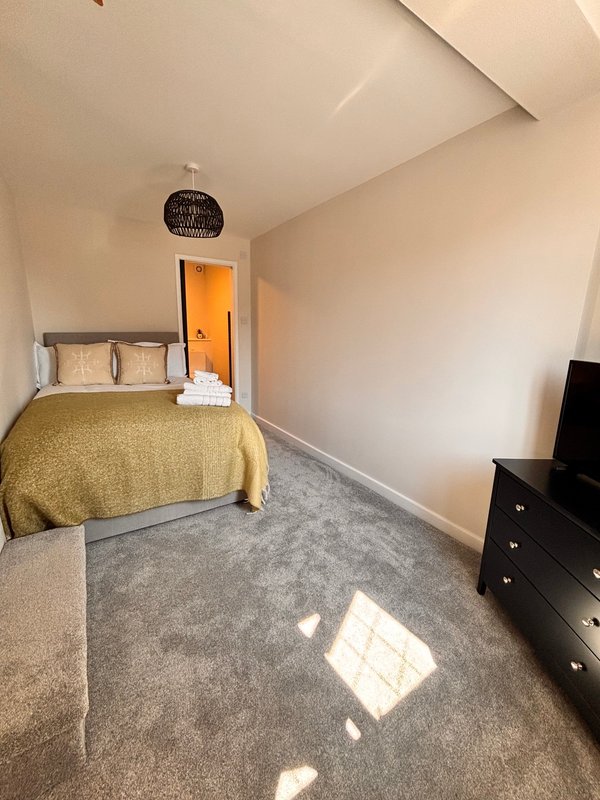 Compact bedroom with single bed, yellow bedspread, dark dresser, and grey carpet flooring